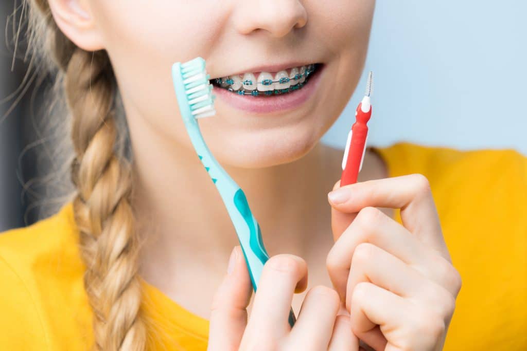 Dentist and orthodontist concept. Young woman smiling cleaning and brushing teeth with braces using toothbrush